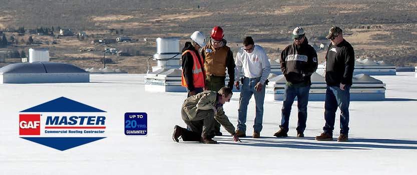 Workers observing another worker pointing to a spot on a commercial roof with the GAF Master Commercial Roofing Contractor logo on the left hand side