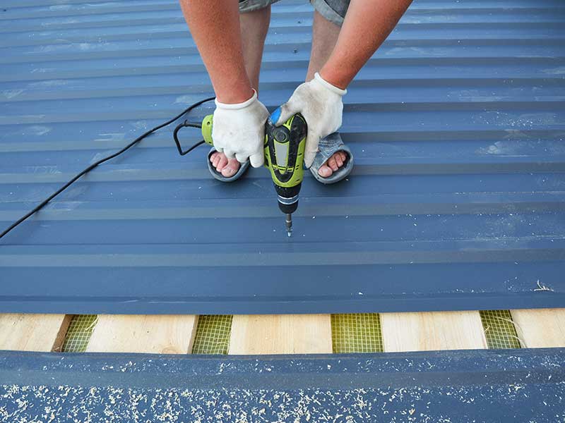 Close-up of worker using a drill to install metal roof panels