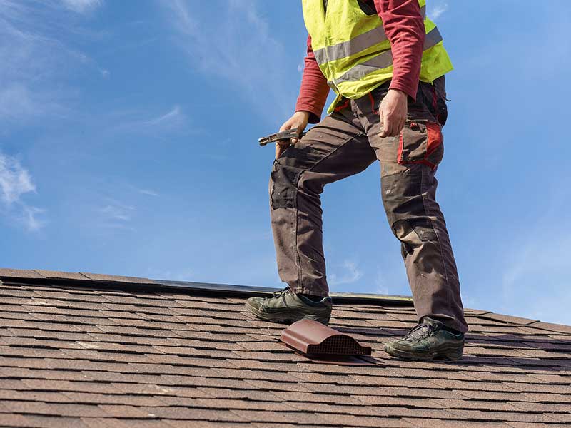Worker inspecting the top of a residential roof with brown asphalt shingles